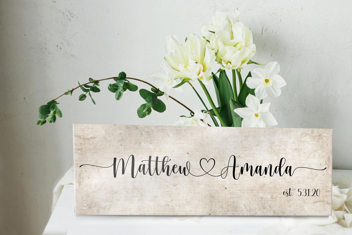 rustic cotton canvas name sign, with 2 first names connected by a heart in a whimsical and playful typeface. A personalized name sign on vintage cotton hangs on wall above bench in entry of home.