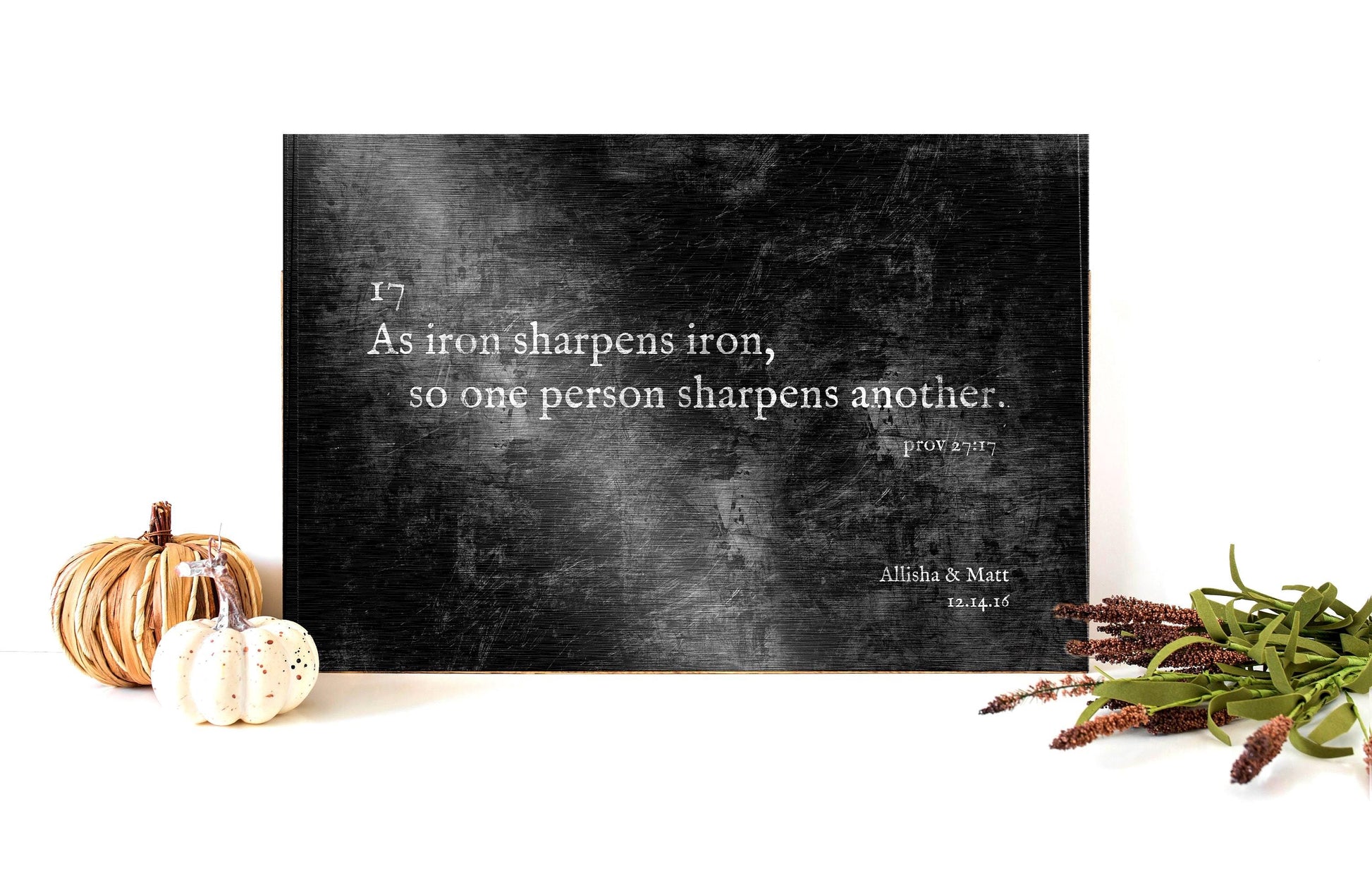 Men’s Christian black, rustic metal iron theme artwork featuring Proverbs 2717, as iron sharpens iron so one person sharps in other Bible verse. Plaque is set on table top with full theme accents.