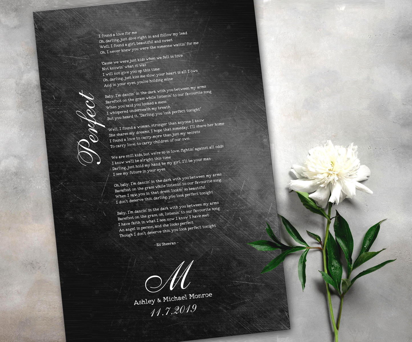 Iron anniversary gifts like this distressed metal song plaque featuring personalized song lyrics, a couple's name and anniversary date are becoming very popular for husband and wife anniversaries. The rustic and distressed affect give this keepsake a rugged feel while also blending a touch of elegance and whimsy with it's thoughtful font pairing of vintage type writer and calligraphy. A white rose sits beside the plaque which is laying on a table top.