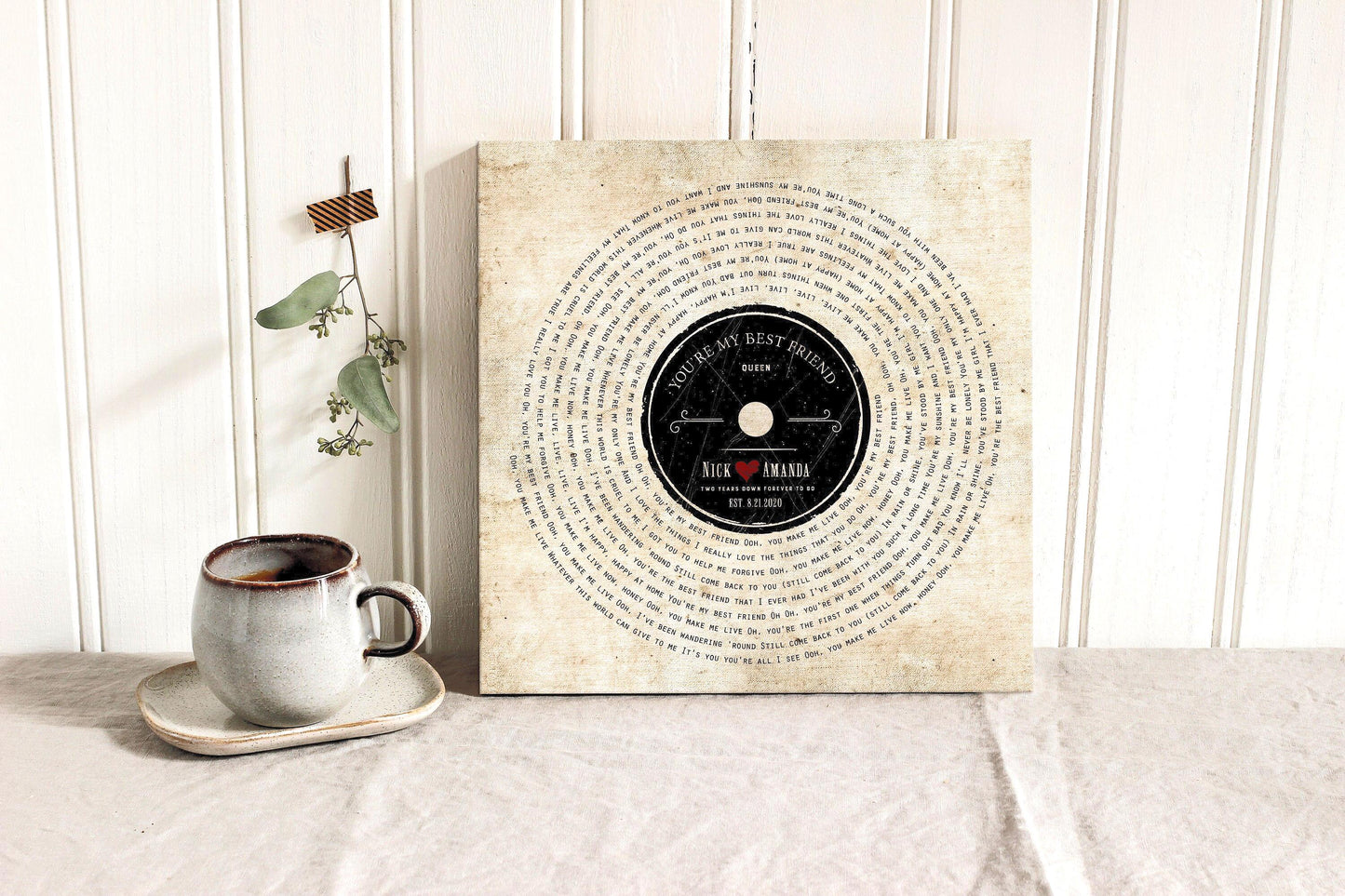 Retro Vinyl song lyrics canvas with custom song lyrics, couple's names and established date. Popular 2 year anniversary gift for traditional cotton gifts. Canvas couple's art features any song lyrics. Set on a neutral background with a cup of tea, on a table draped with cotton cloth.