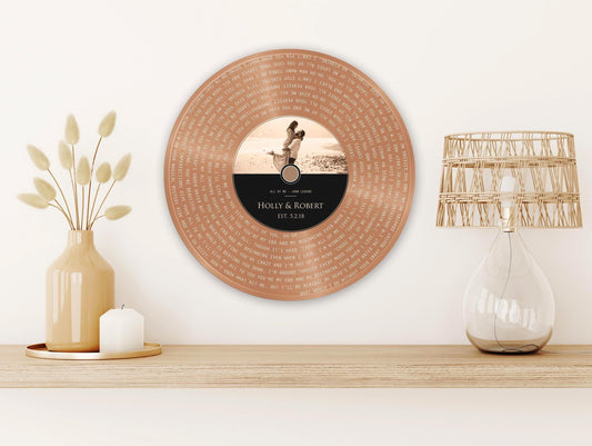 Metal vinyl record wall decor or plaque featured in copper with a personalized inscription for Holly & Robert, established in 2018. The record features a photo of a couple on the label. The song lyrics of their wedding song are inscribed into the copper "vinyl" portion of the record.