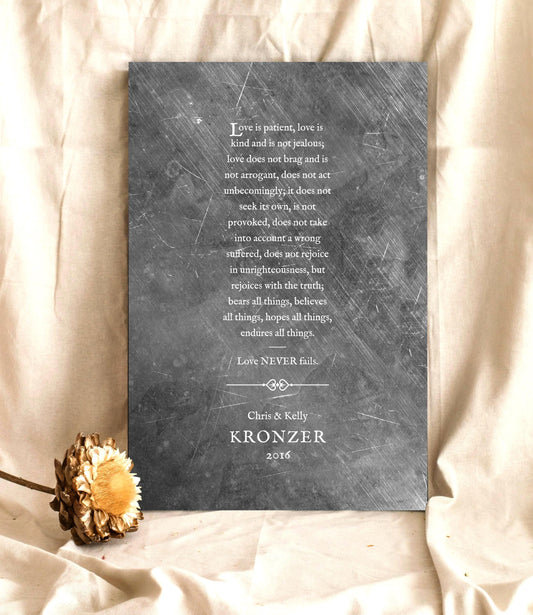 Personalized Tin 1 Corinthians 13 Tin Anniversary Plaque for couples is handcrafted on aluminum alloyed tin, distressed and inscribed with the classic Love is patient, love is kind reading in old-world lettering. A decorative divider with rustic hearts separates the reading from the personalization of the names of a couple and their established date. 
Plaque is set on a platform covered in a cream-toned sheeting with a flower in the bottom left corner.

Photo courtesy of Honeycomb Proverbs