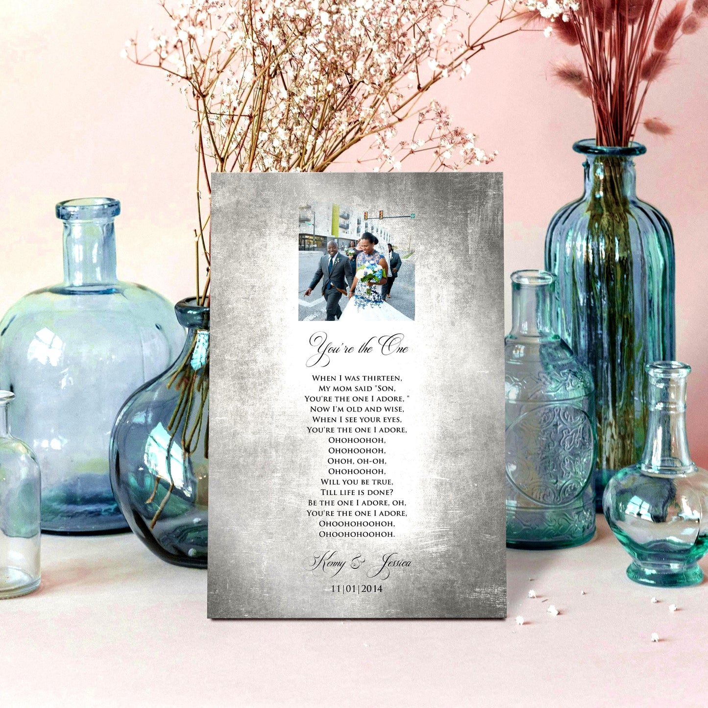 Custom Portrait plaque on tin for couples. Features the song lyrics or wording of choice and a photo cameo above the lyrics. This piece is handcrafted on vintage tin and is displayed with vases on a pale pink background.

Courtesy of Honeycomb Proverbs